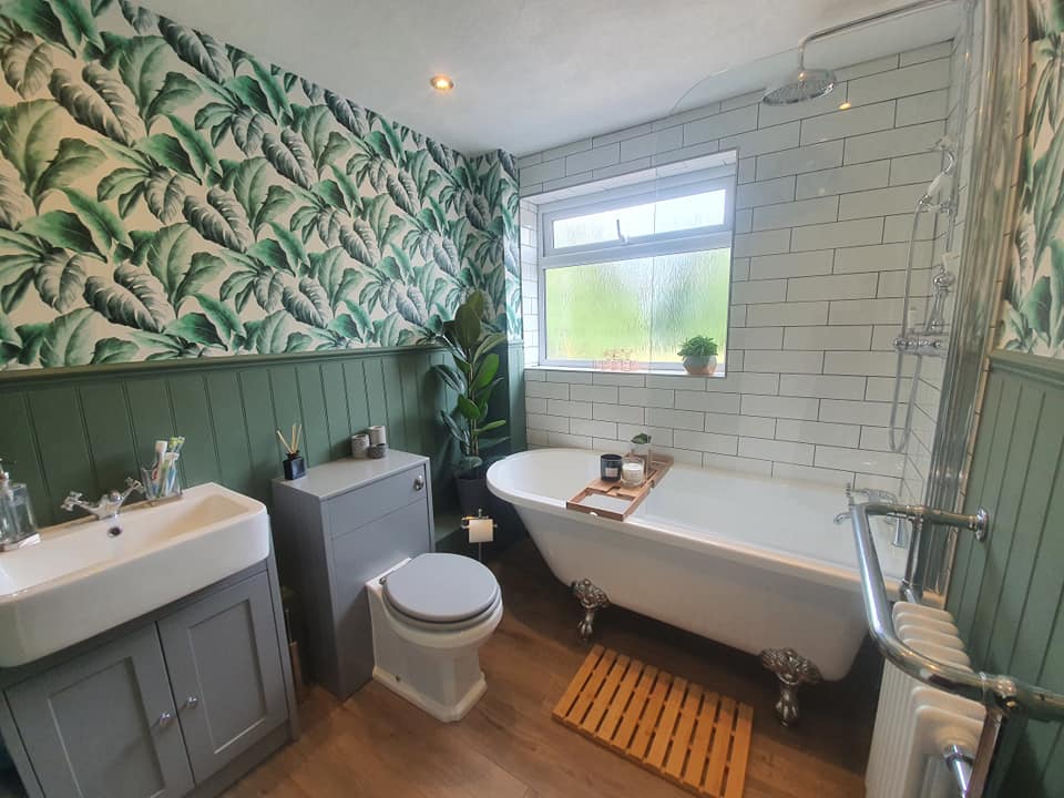 Bathroom with a roll-top claw-foot bath, palm-leaf wallpaper, green panelling and metro tiles