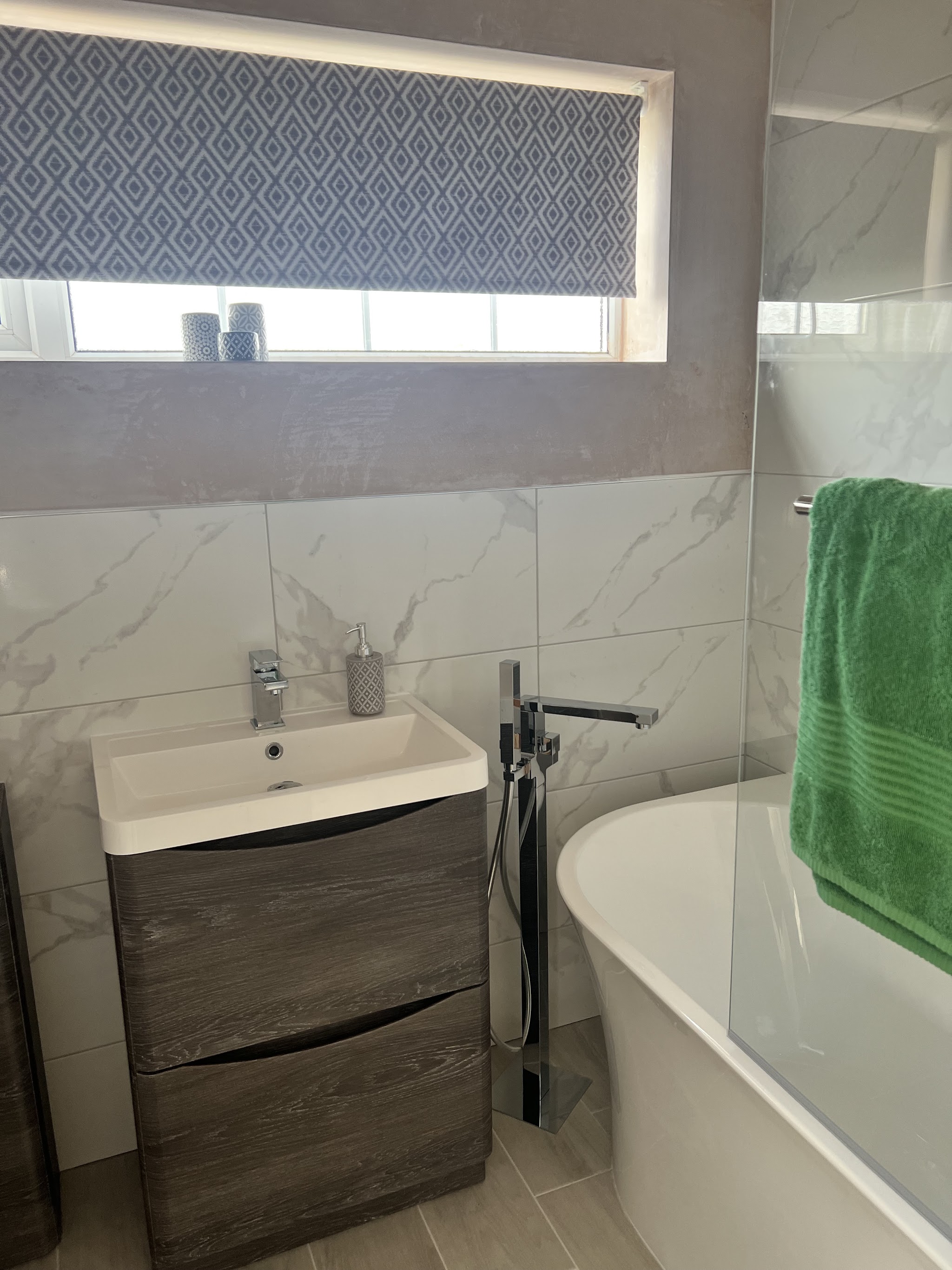 Finished bathroom with marble-effect tiles, a freestanding bath tap and a wood-effect vanity