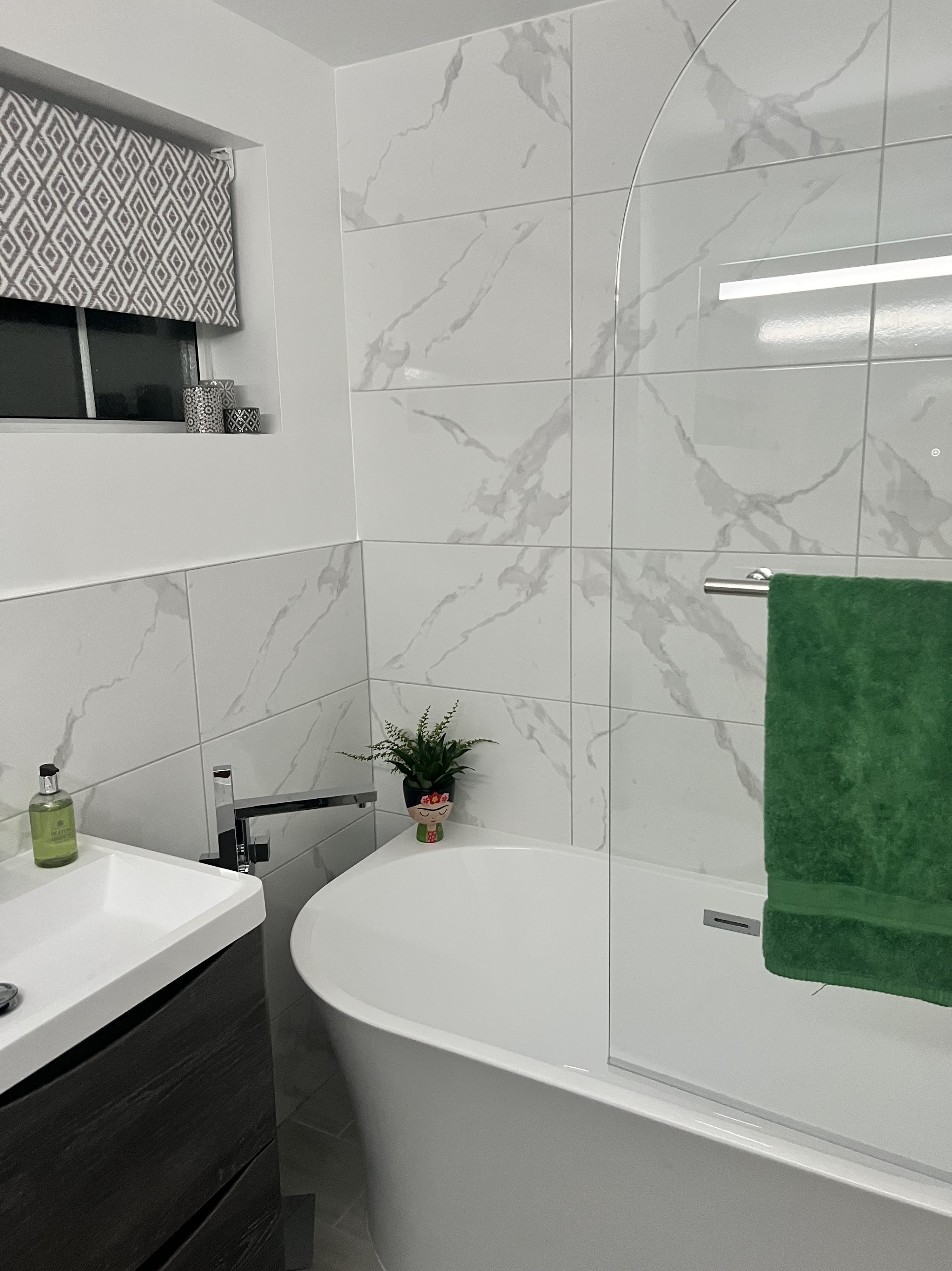 Bath with a glass screen and marble-effect wall tiles